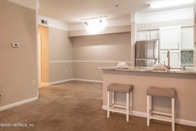 kitchen with stainless steel refrigerator, white cabinetry, rail lighting, a breakfast bar area, and ornamental molding