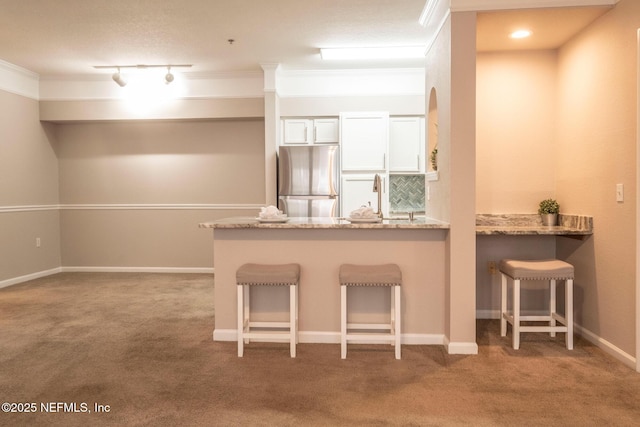 kitchen with crown molding, stainless steel refrigerator, white cabinetry, a kitchen bar, and kitchen peninsula