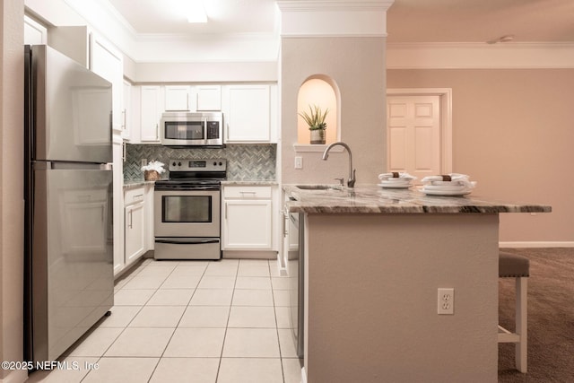 kitchen with light tile patterned floors, a peninsula, a sink, stainless steel appliances, and a kitchen bar