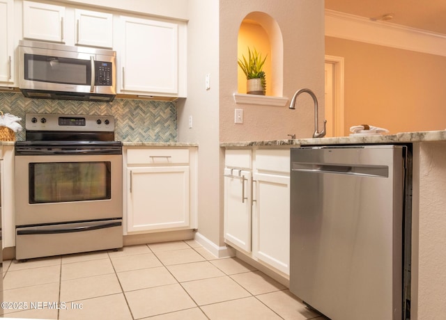 kitchen with light tile patterned flooring, appliances with stainless steel finishes, white cabinetry, decorative backsplash, and ornamental molding