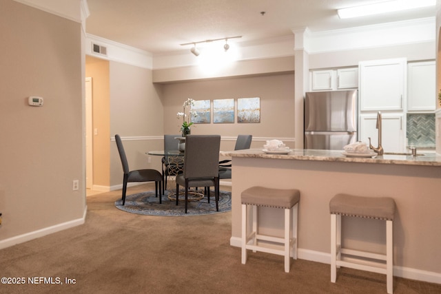 kitchen featuring a breakfast bar area, visible vents, freestanding refrigerator, ornamental molding, and carpet flooring