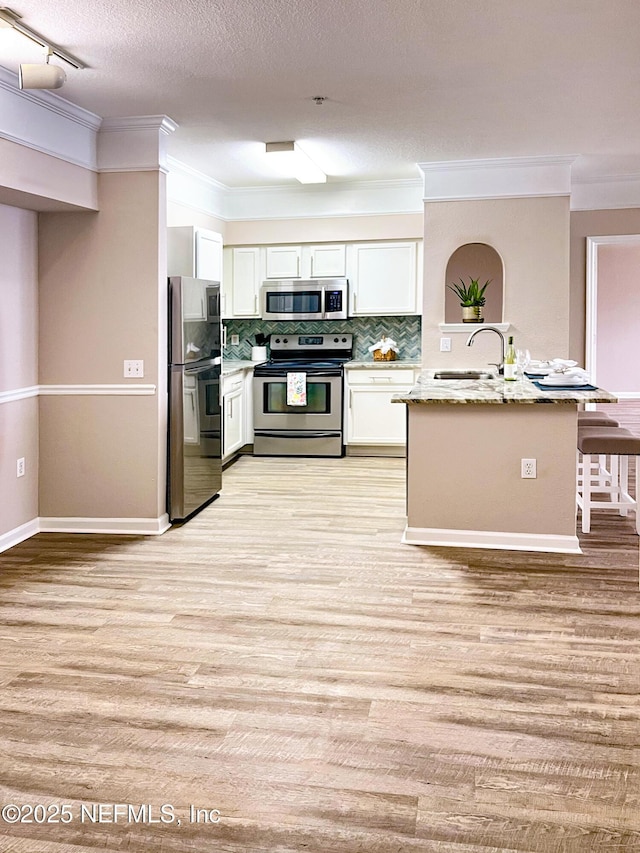 kitchen with appliances with stainless steel finishes, white cabinetry, light wood-type flooring, and a sink