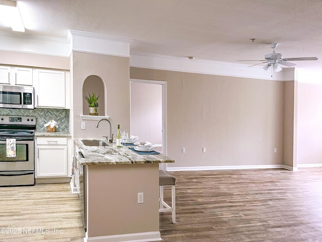 kitchen featuring light wood finished floors, a kitchen bar, a peninsula, stainless steel appliances, and a sink