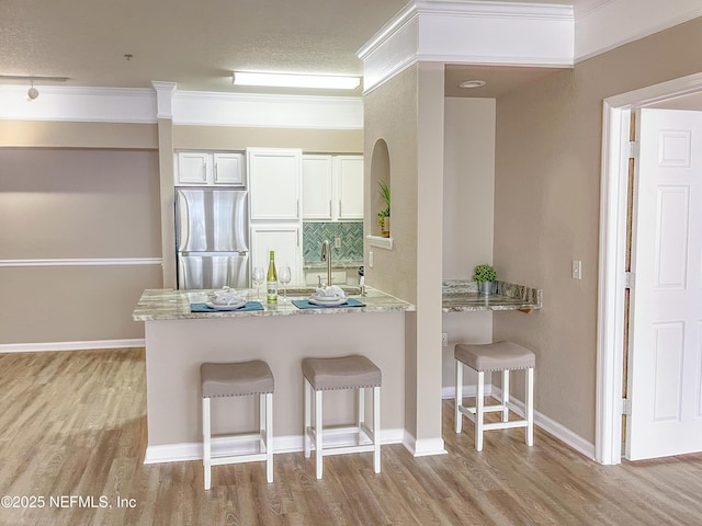 kitchen featuring a breakfast bar, a peninsula, light wood-type flooring, and stainless steel refrigerator