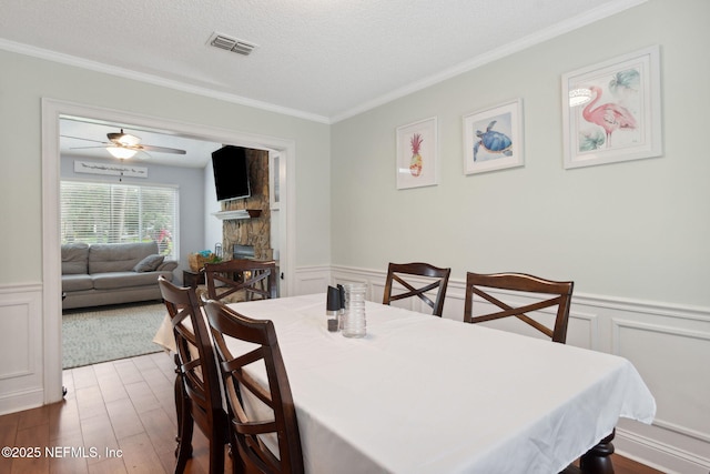 dining room featuring hardwood / wood-style flooring, ceiling fan, a fireplace, a textured ceiling, and ornamental molding