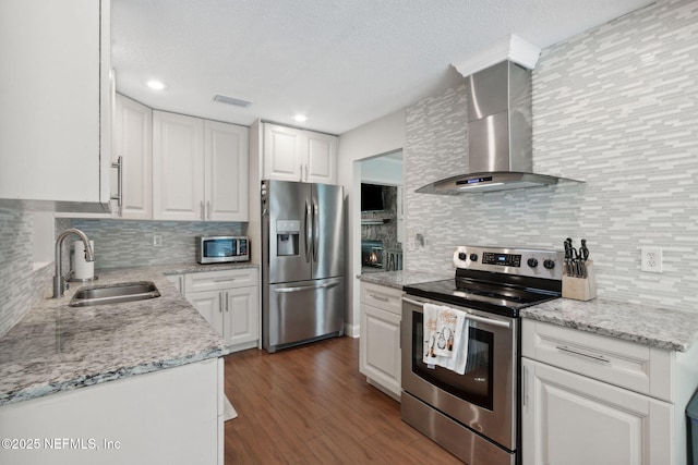 kitchen with stainless steel appliances, sink, white cabinets, and wall chimney range hood