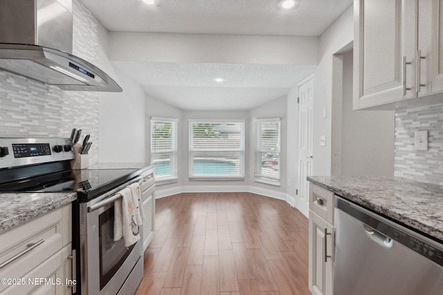 kitchen with white cabinetry, appliances with stainless steel finishes, decorative backsplash, light stone countertops, and range hood