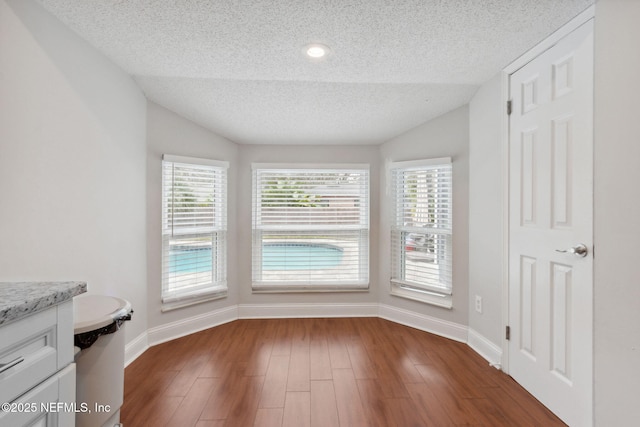 unfurnished dining area with a textured ceiling, dark hardwood / wood-style flooring, and vaulted ceiling