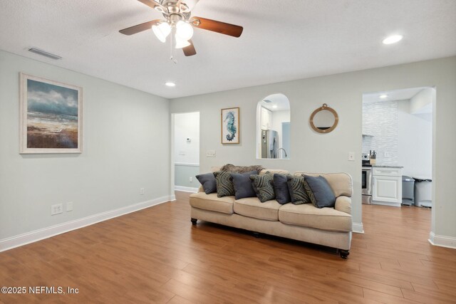 living room featuring ceiling fan, a textured ceiling, and light hardwood / wood-style flooring