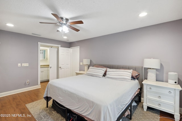 bedroom featuring a textured ceiling, ceiling fan, ensuite bathroom, and dark hardwood / wood-style flooring