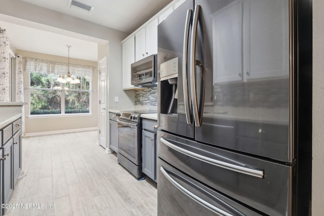 kitchen with tasteful backsplash, white cabinetry, gray cabinetry, a chandelier, and stainless steel appliances