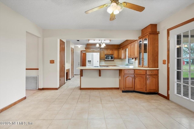 kitchen featuring white fridge with ice dispenser, light tile patterned floors, ceiling fan, kitchen peninsula, and a textured ceiling