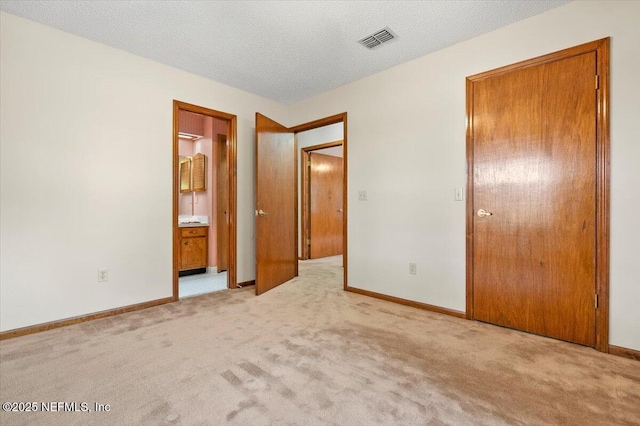 unfurnished bedroom with connected bathroom, light carpet, and a textured ceiling