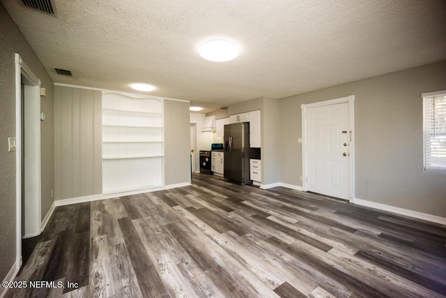 unfurnished living room featuring built in shelves, a textured ceiling, and dark hardwood / wood-style floors