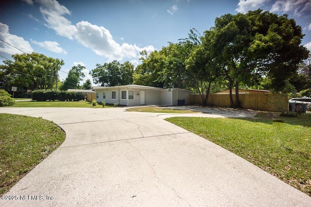 view of front of house featuring curved driveway, fence, and a front lawn