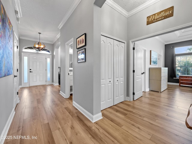 foyer entrance with ornamental molding, a textured ceiling, and light hardwood / wood-style floors