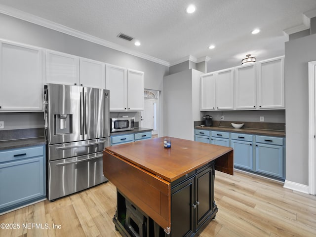 kitchen with blue cabinets, white cabinetry, a textured ceiling, ornamental molding, and appliances with stainless steel finishes