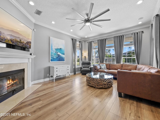 living room with crown molding, a fireplace, a textured ceiling, and light wood-type flooring