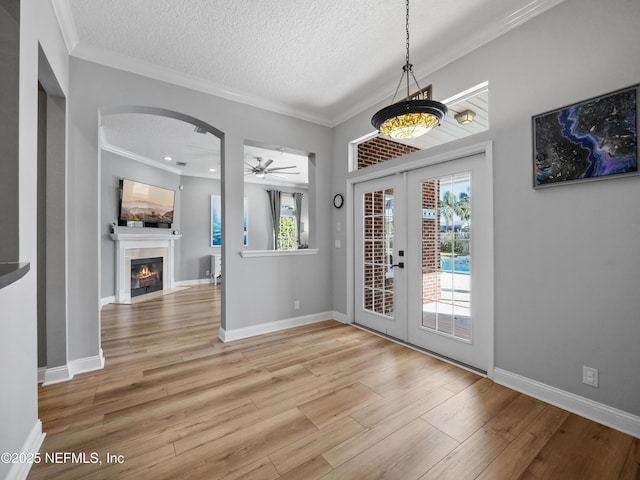 foyer entrance with french doors, ornamental molding, ceiling fan, a textured ceiling, and light hardwood / wood-style flooring