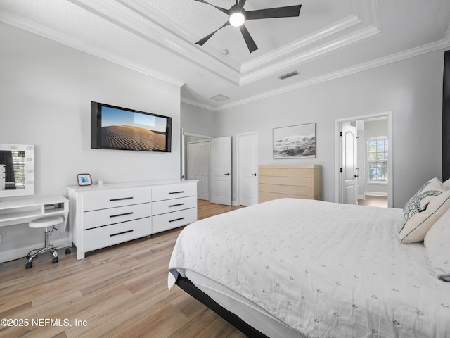 bedroom with crown molding, ceiling fan, a tray ceiling, light hardwood / wood-style floors, and a textured ceiling