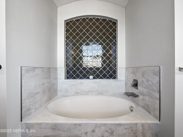 bathroom with a relaxing tiled tub and a textured ceiling