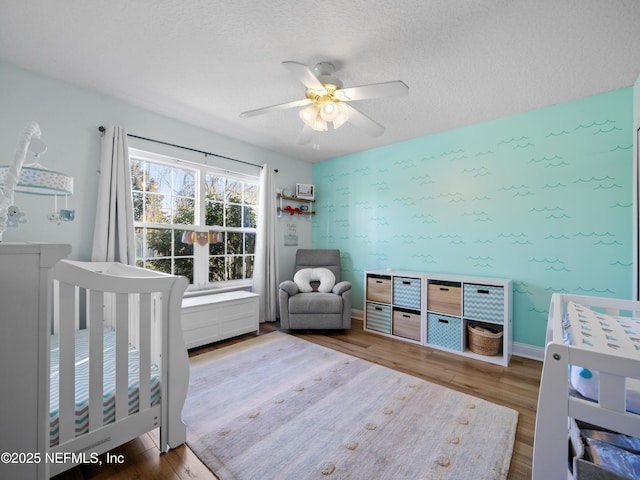 bedroom featuring hardwood / wood-style flooring, a crib, a textured ceiling, and ceiling fan