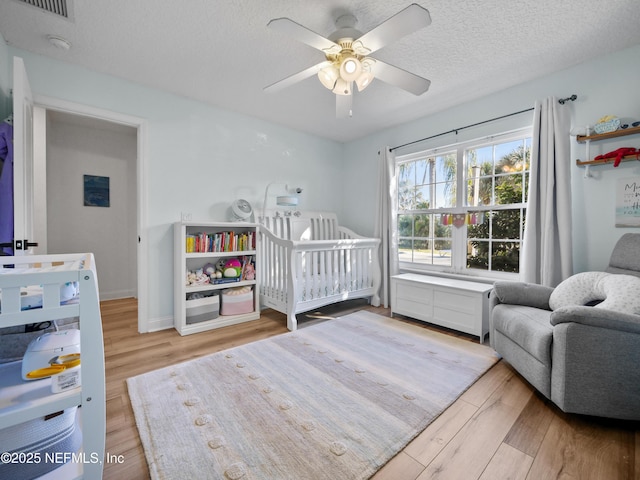 bedroom featuring hardwood / wood-style flooring, a textured ceiling, a nursery area, and ceiling fan