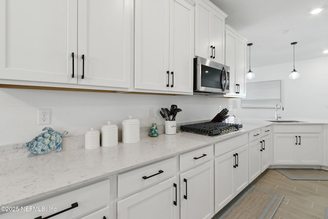 kitchen featuring decorative light fixtures, sink, stainless steel appliances, white cabinets, and light stone counters