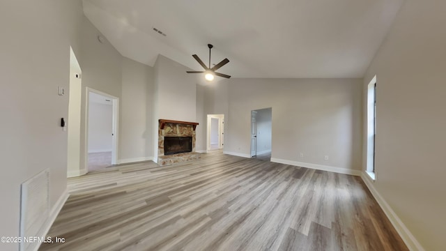 unfurnished living room featuring high vaulted ceiling, ceiling fan, a stone fireplace, and light hardwood / wood-style floors