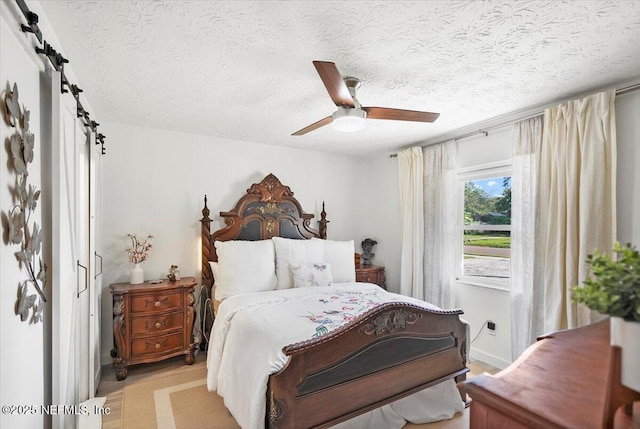 bedroom with ceiling fan, a barn door, and a textured ceiling