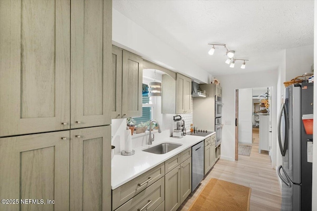 kitchen with appliances with stainless steel finishes, sink, light hardwood / wood-style floors, a textured ceiling, and wall chimney exhaust hood