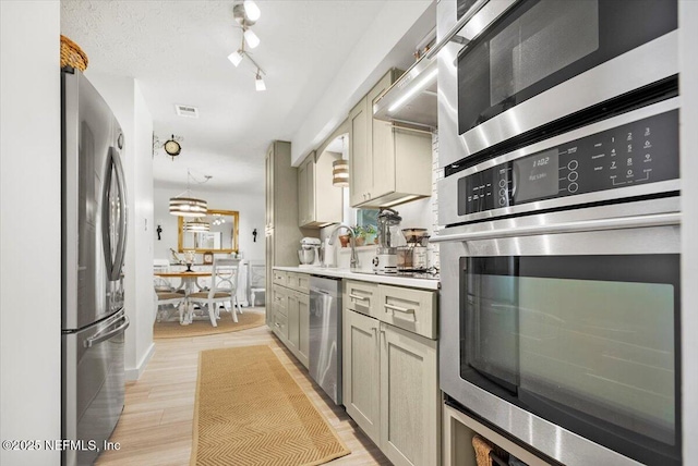 kitchen featuring cream cabinets, stainless steel appliances, rail lighting, and light hardwood / wood-style floors