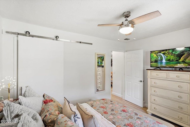 bedroom with ceiling fan, light hardwood / wood-style floors, a barn door, and a textured ceiling