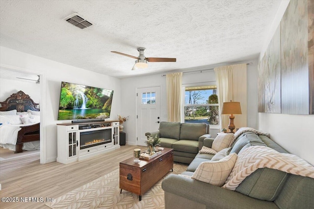 living room with ceiling fan, light hardwood / wood-style floors, and a textured ceiling