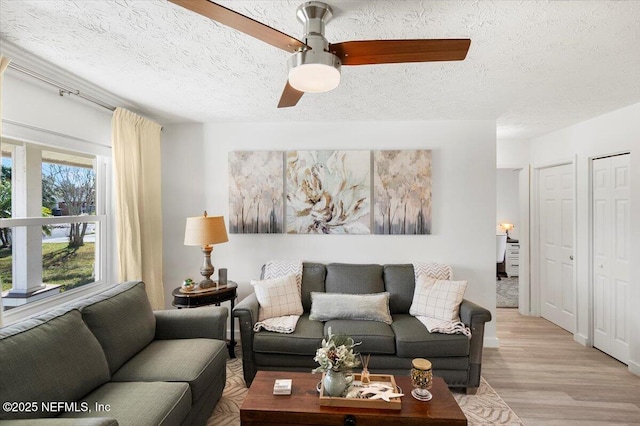 living room with ceiling fan, a textured ceiling, and light wood-type flooring