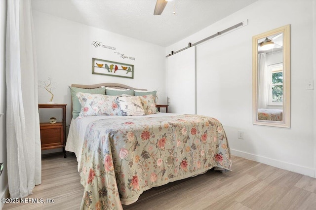 bedroom featuring ceiling fan, a barn door, a textured ceiling, and light wood-type flooring