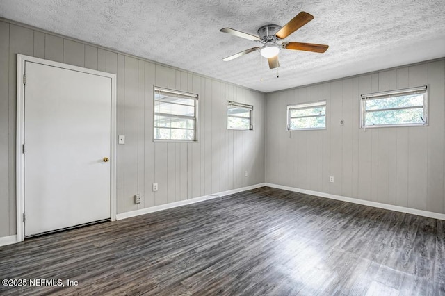 empty room with ceiling fan, dark wood-type flooring, wood walls, and a textured ceiling