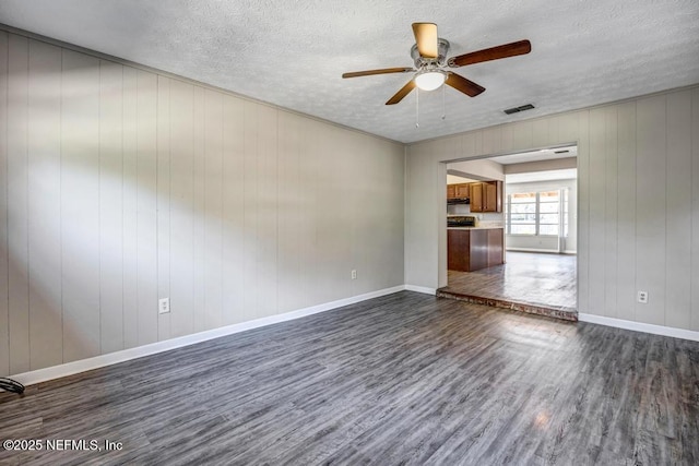 unfurnished room with ceiling fan, a textured ceiling, dark hardwood / wood-style floors, and wooden walls