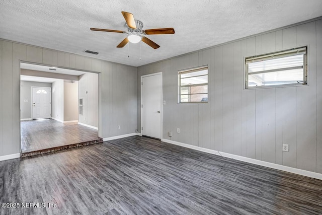 unfurnished room featuring ceiling fan, a textured ceiling, dark hardwood / wood-style floors, and wood walls