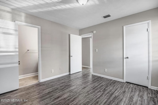 unfurnished bedroom with a spacious closet and dark hardwood / wood-style flooring