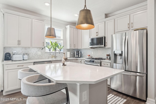 kitchen with appliances with stainless steel finishes, hanging light fixtures, tasteful backsplash, white cabinets, and a kitchen island