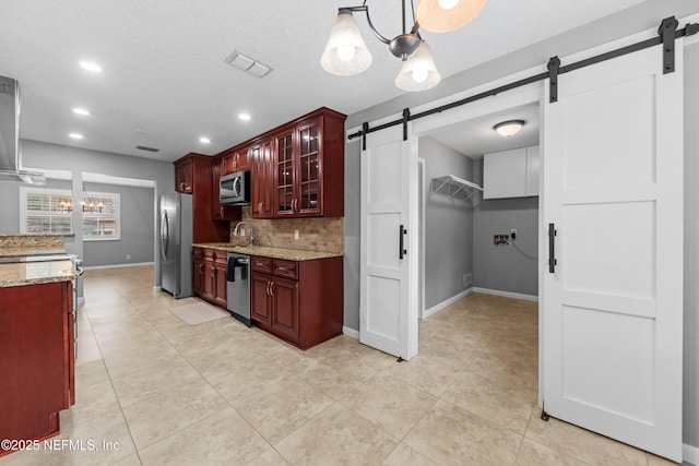 kitchen featuring light stone countertops, appliances with stainless steel finishes, decorative light fixtures, tasteful backsplash, and a barn door