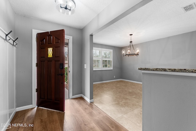 entrance foyer featuring light wood-type flooring, an inviting chandelier, and a textured ceiling