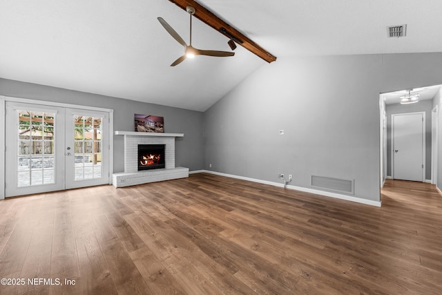 unfurnished living room with wood-type flooring, french doors, a fireplace, lofted ceiling with beams, and ceiling fan