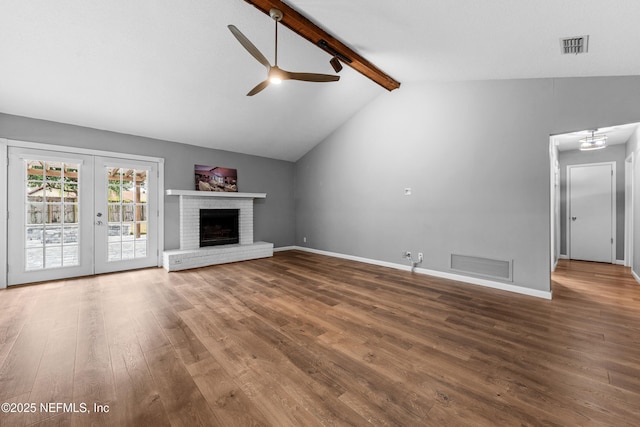 unfurnished living room featuring ceiling fan, french doors, a fireplace, hardwood / wood-style floors, and vaulted ceiling with beams