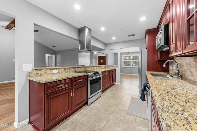 kitchen with island exhaust hood, light tile patterned floors, sink, stainless steel appliances, and light stone counters