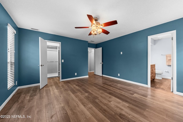 unfurnished bedroom with ensuite bathroom, a spacious closet, a closet, dark hardwood / wood-style flooring, and ceiling fan