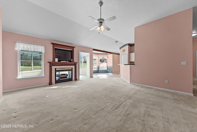 unfurnished living room with lofted ceiling, a tiled fireplace, ceiling fan, light carpet, and a textured ceiling