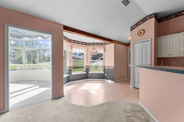 kitchen with pendant lighting, white cabinetry, a textured ceiling, light colored carpet, and beamed ceiling