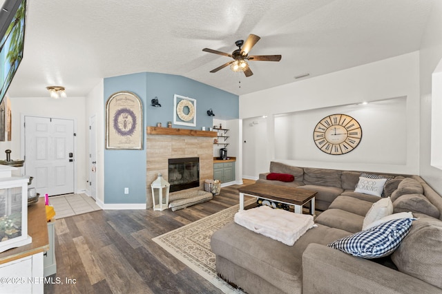 living room with lofted ceiling, a textured ceiling, a tile fireplace, hardwood / wood-style flooring, and ceiling fan